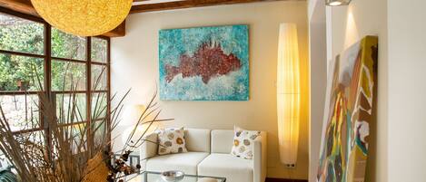 A living room with a sofa, a glass coffee table, and a painting on the wall.