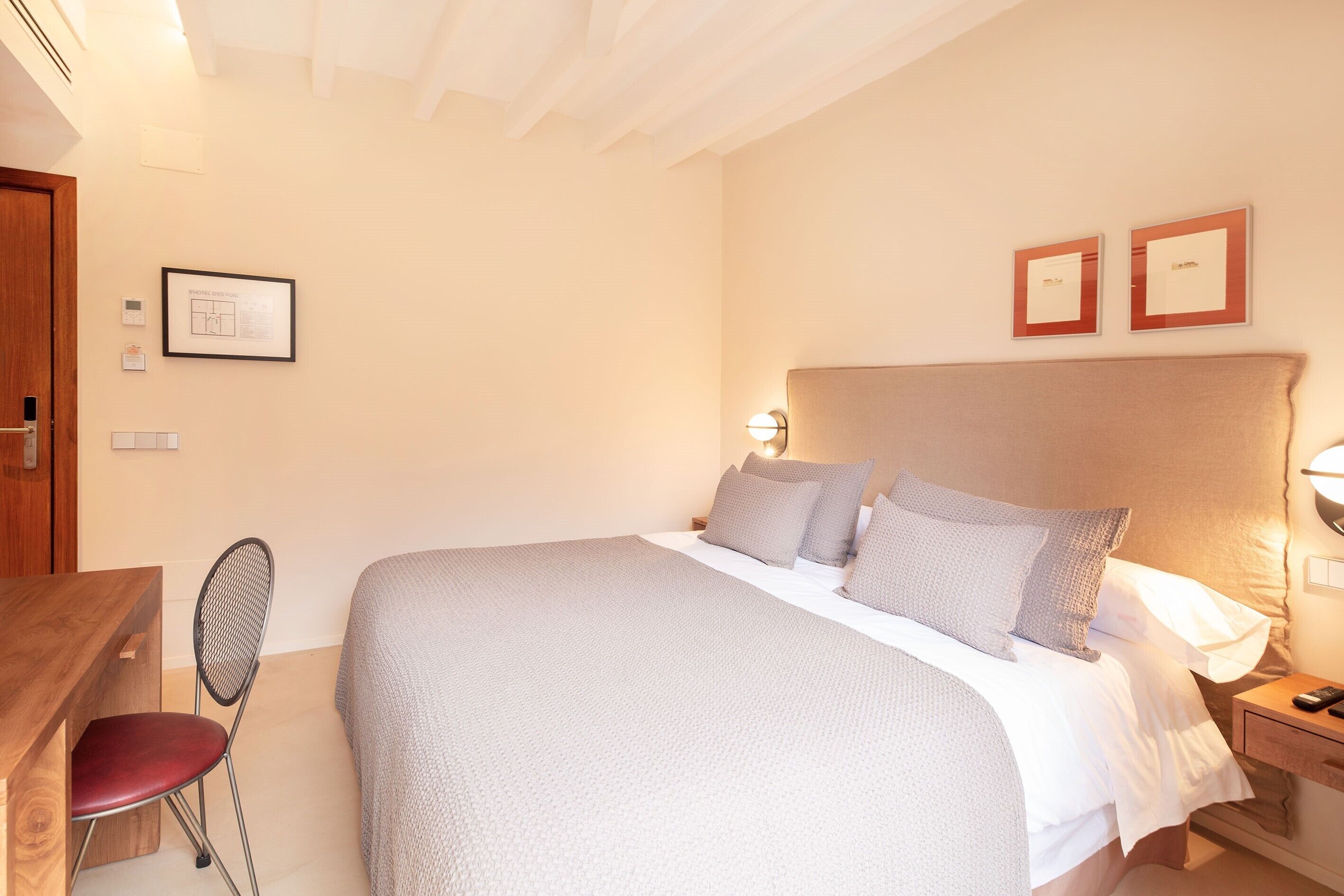 Une chambre bien rangée, avec un lit, une table de chevet, une chaise et une lampe fixée au mur.