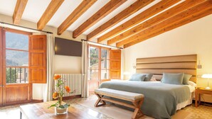Une chambre avec un plafond en bois, un grand lit avec une literie verte, un banc, une table avec un vase de fleurs et un téléviseur fixé au mur.