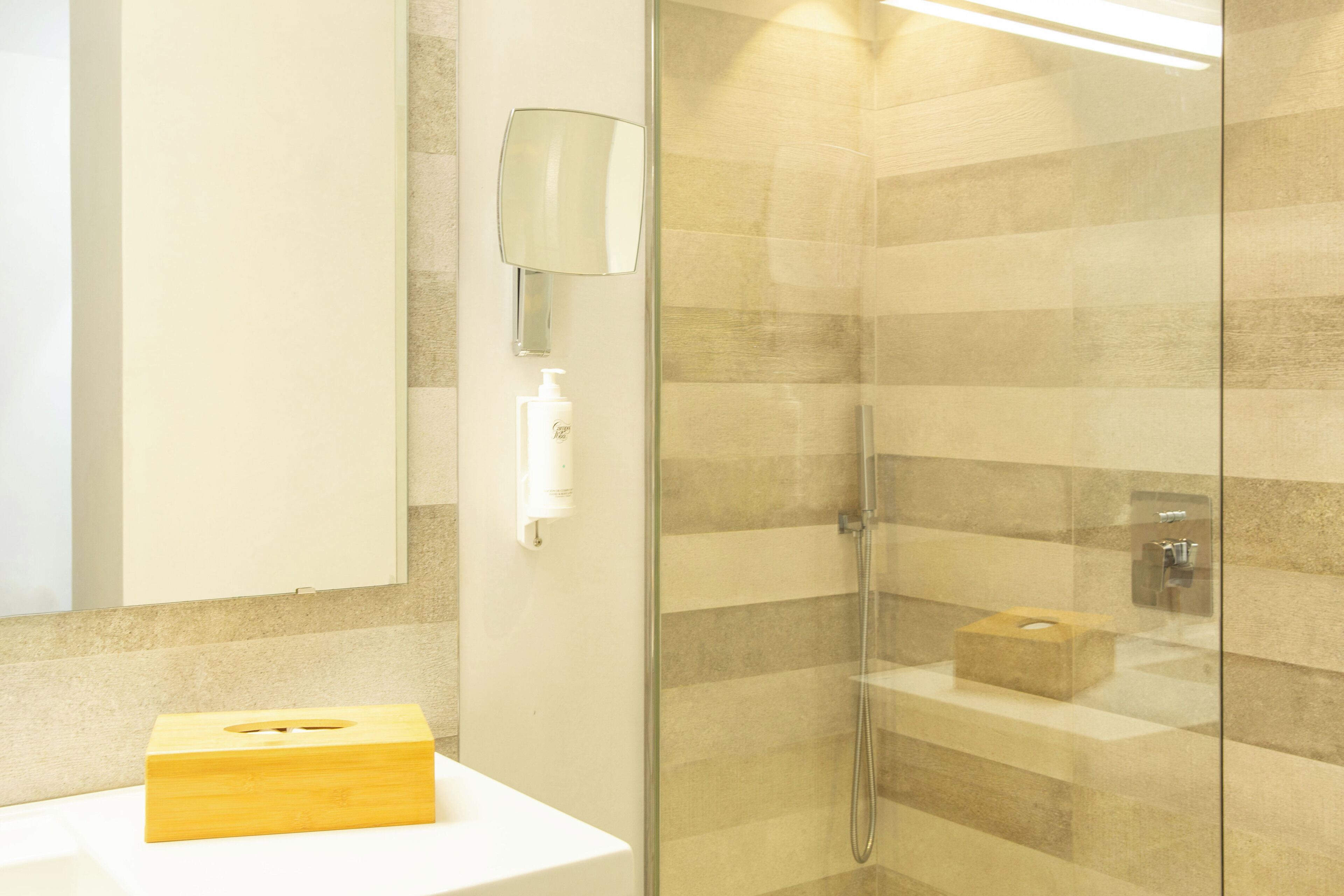 Un baño moderno con cabina de ducha de vidrio, un lavabo blanco, un espejo y dispensador de jabón.