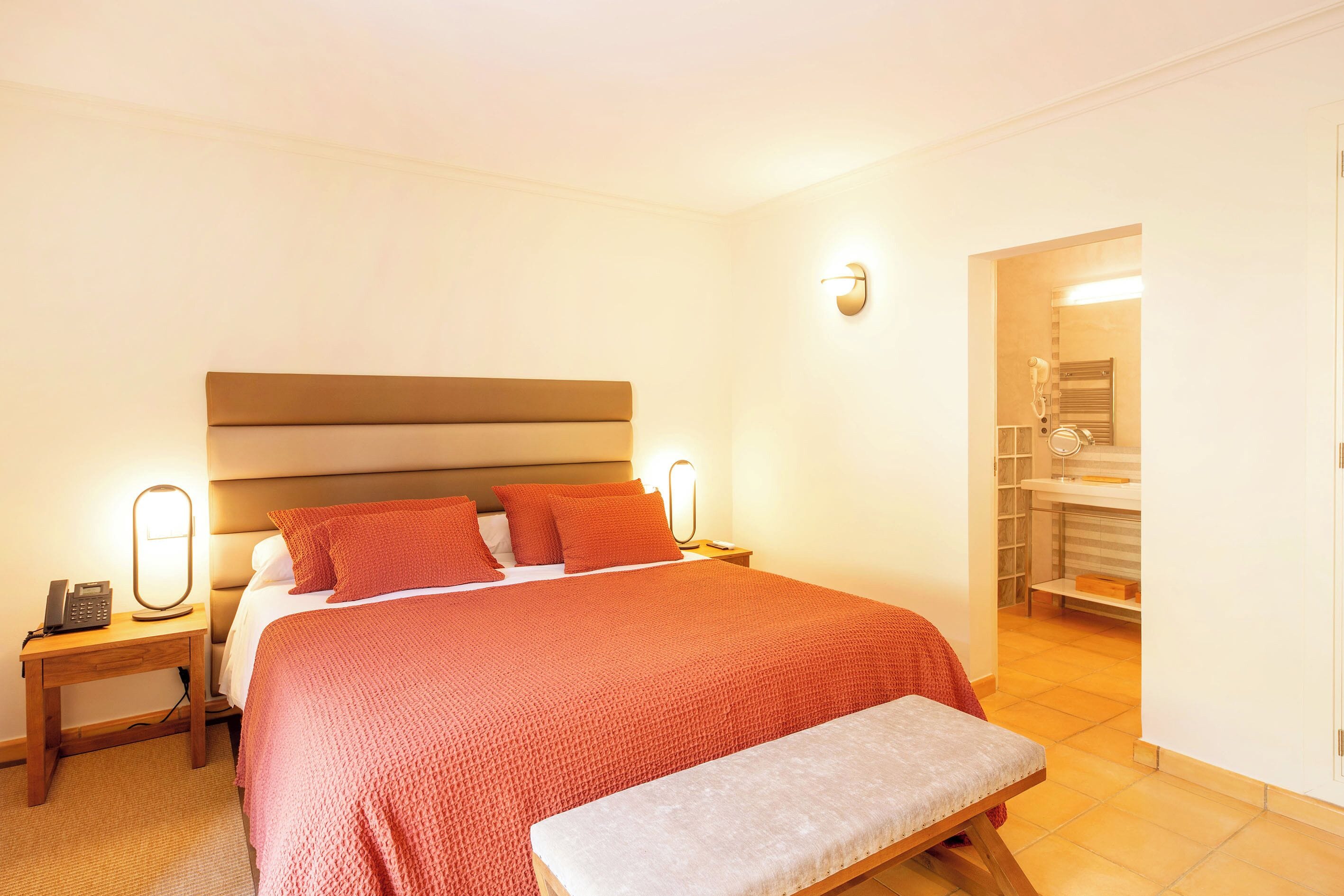 A hotel room with a large bed, bedside lamps, a bedside phone, and a bathroom visible through an open door.
