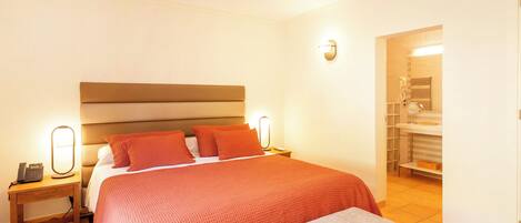 A hotel room with a large bed, bedside lamps, a bedside phone, and a bathroom visible through an open door.