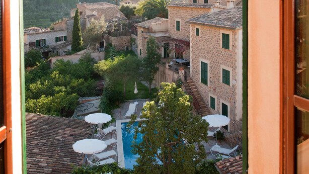 Une vue depuis une fenêtre donnant sur une cour intérieure avec une piscine, des espaces de détente en plein air et des bâtiments traditionnels.