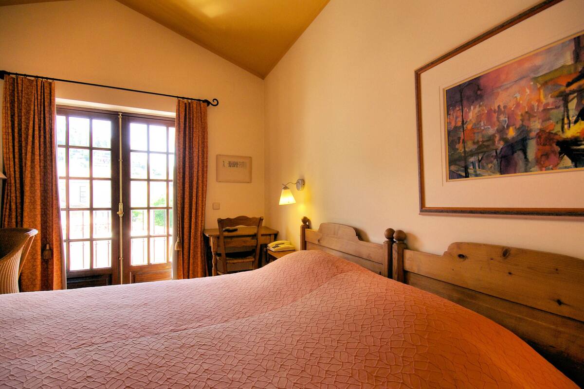 A hotel room with a large bed, a wooden headboard, a desk with a chair, a lamp, and a painting on the wall.