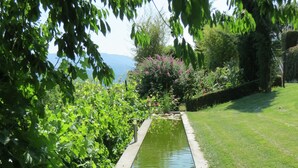 A garden with a narrow water feature, lush greenery, and a view of the sea. - Hotel Rural Quinta da Geia (Oliveira do Hospital)
