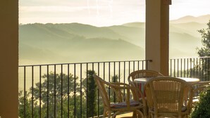 A balcony with wicker chairs and a table, overlooking a mountainous landscape. - Hotel Rural Quinta da Geia (Oliveira do Hospital)