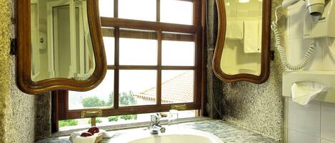 Un baño con lavamanos, dos espejos, una ventana y un secador de pelo en la pared.