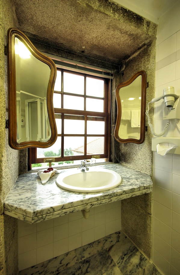 A bathroom with a sink, two mirrors, a window, and a hairdryer on the wall.