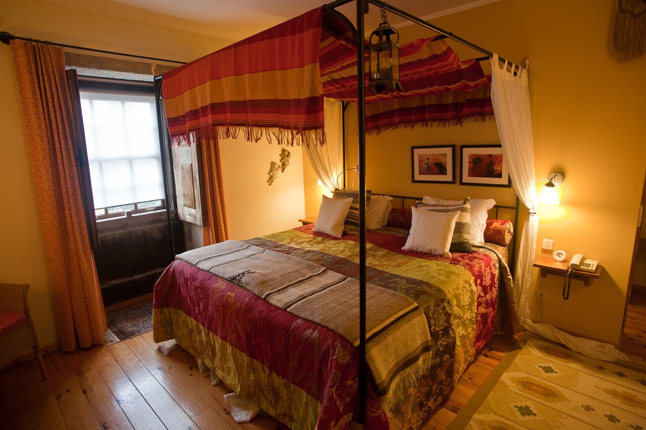 A four-poster bed with a canopy, a bedside table with a lamp, and a telephone on a wall-mounted shelf.