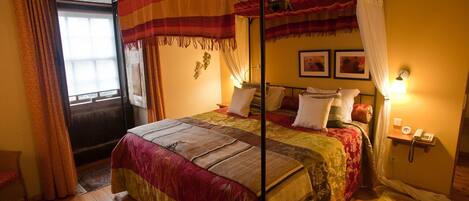 A four-poster bed with a canopy, a bedside table with a lamp, and a telephone on a wall-mounted shelf.