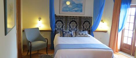 A bedroom with a bed, a chair, a painting, and a door.