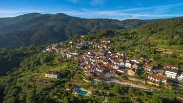 A hillside village with traditional architecture, a central church, and a swimming pool.