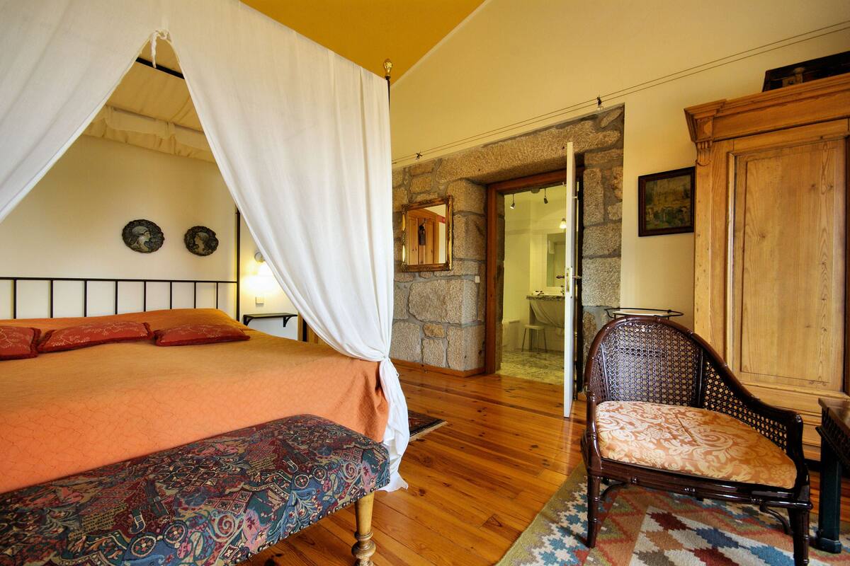 A bedroom with a bed, a chair, a wooden cabinet, and a stone wall.