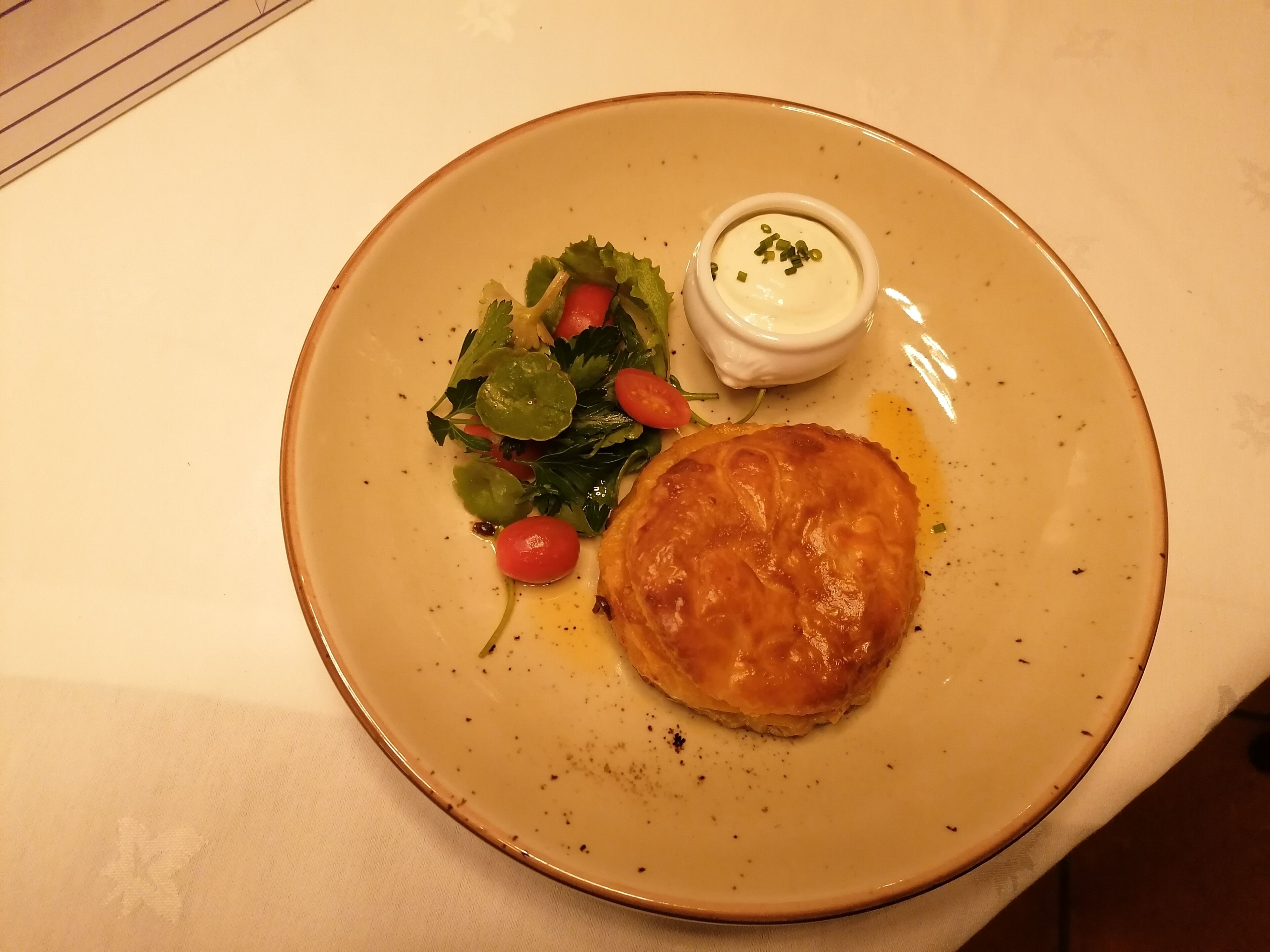 A plate with a pastry, a salad, and a small bowl of sauce.