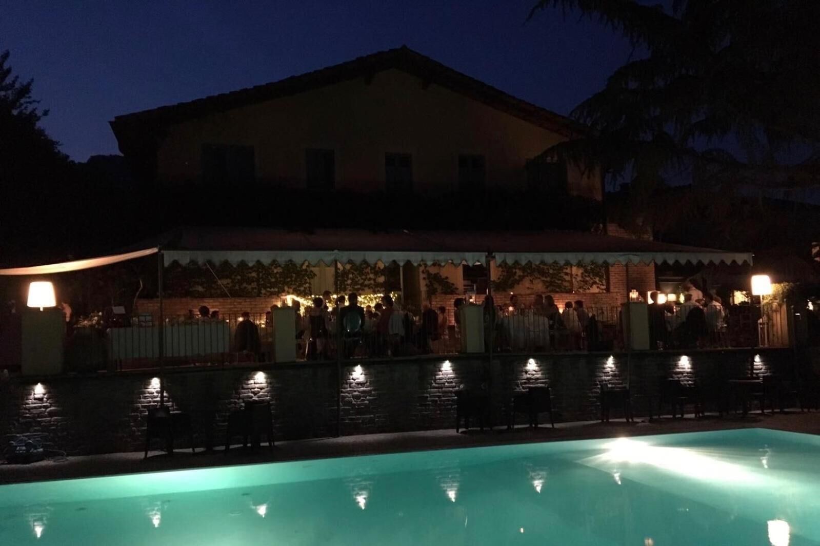 Ein Poolbereich mit einem Gebäude im Hintergrund, einer überdachten Sitzgelegenheit und einem gut beleuchteten Pool.