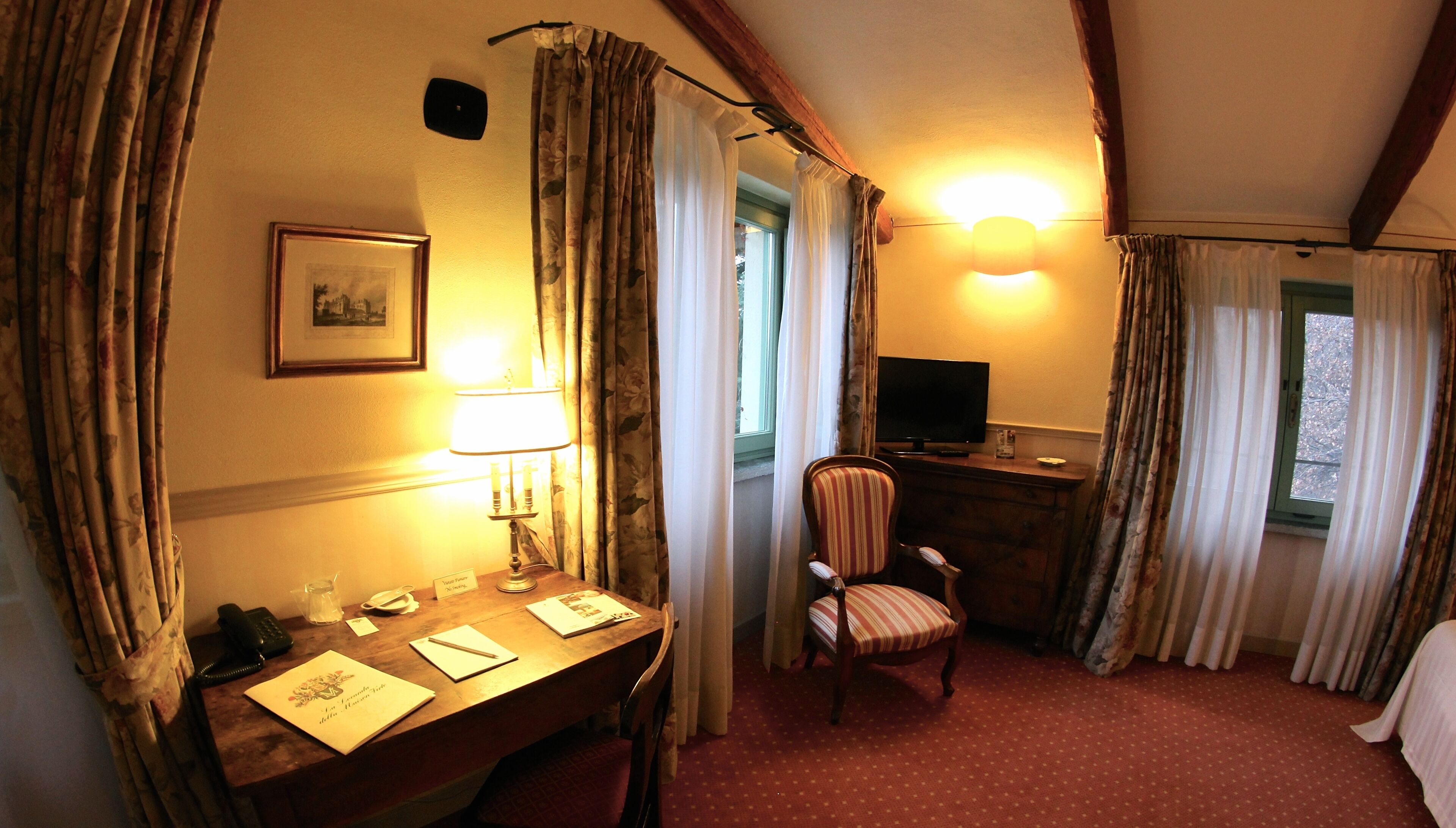 A hotel room with a wooden desk, a chair, a television, and a bed.