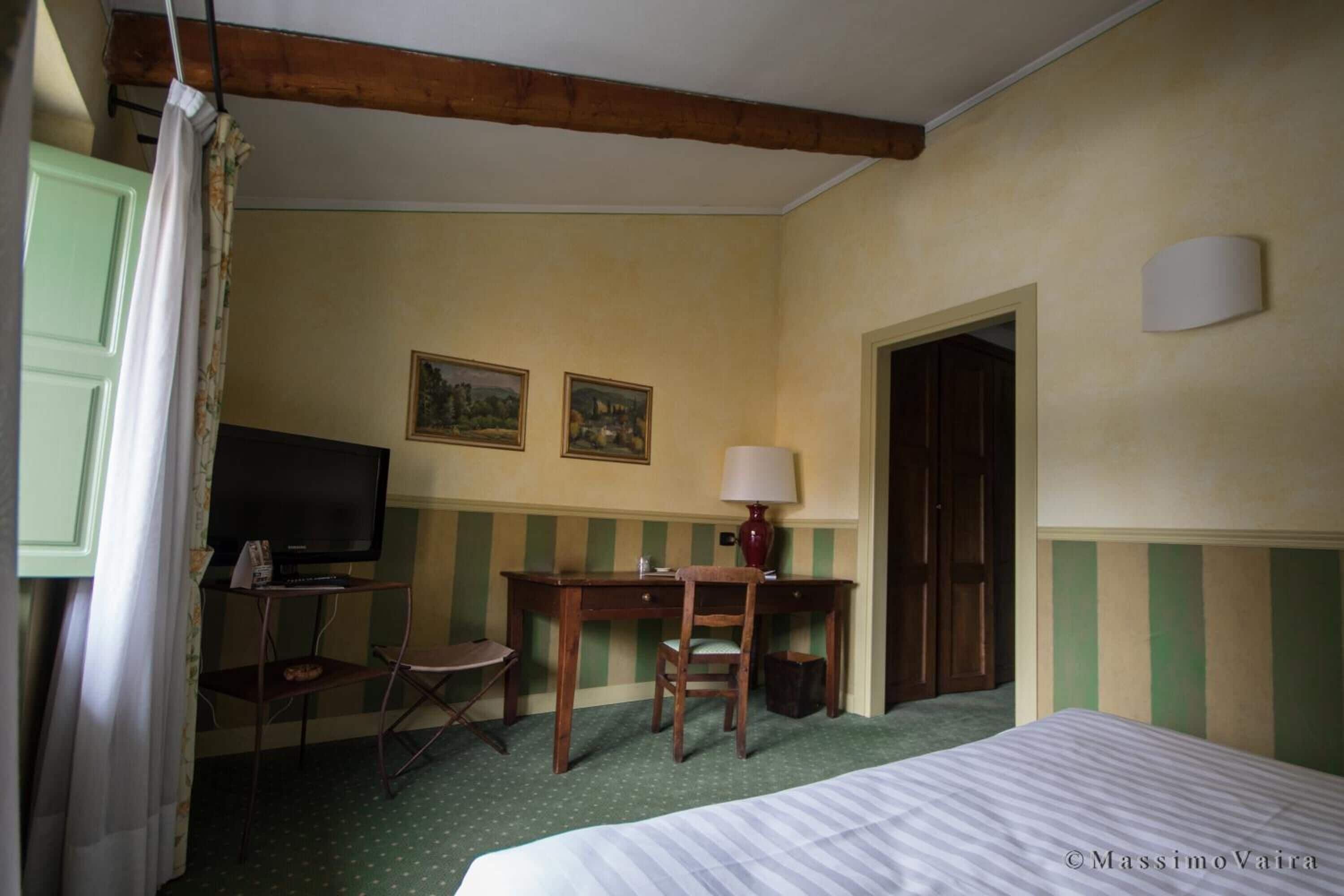 Ein Hotelzimmer mit einem Bett, einem Schreibtisch, einem Stuhl, einem Fernseher und zwei gerahmten Bildern an der Wand.
