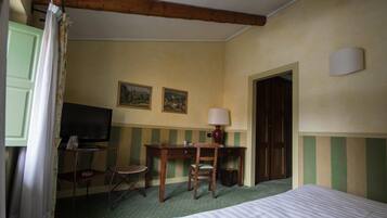 Ein Hotelzimmer mit einem Bett, einem Schreibtisch, einem Stuhl, einem Fernseher und zwei gerahmten Bildern an der Wand.