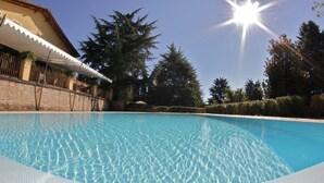 Une piscine aux eaux cristallines, bordée d’une terrasse carrelée, entourée d’un mur de briques, d’arbres et d’un bâtiment doté d’une marquise blanche.