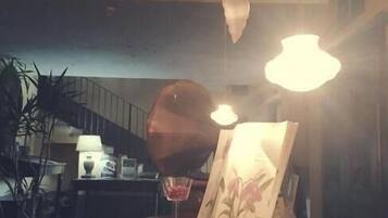Una stanza con un tavolo in legno, una lampada, un bicchiere da bere e un quadro appeso al muro.