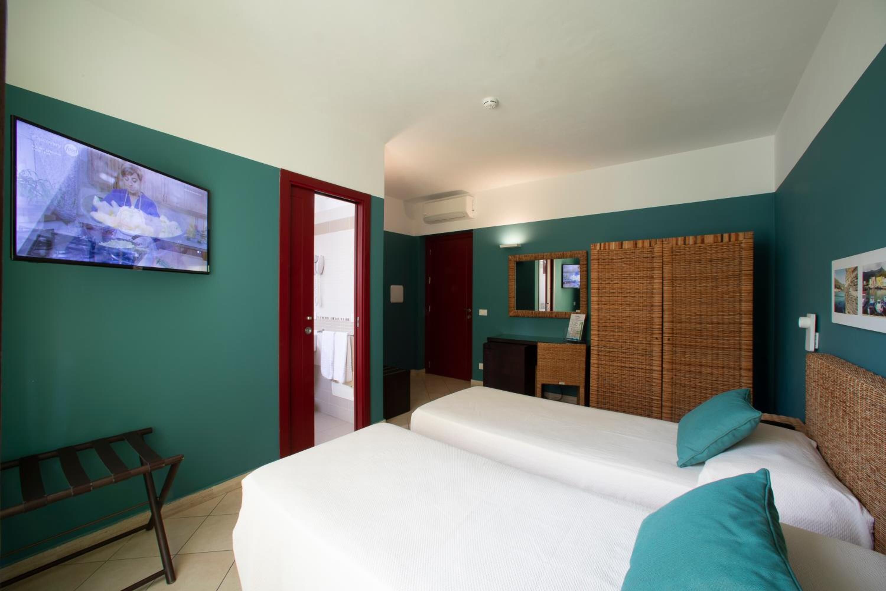 Camera d'albergo con due letti, televisione, bagno e una porta rossa.