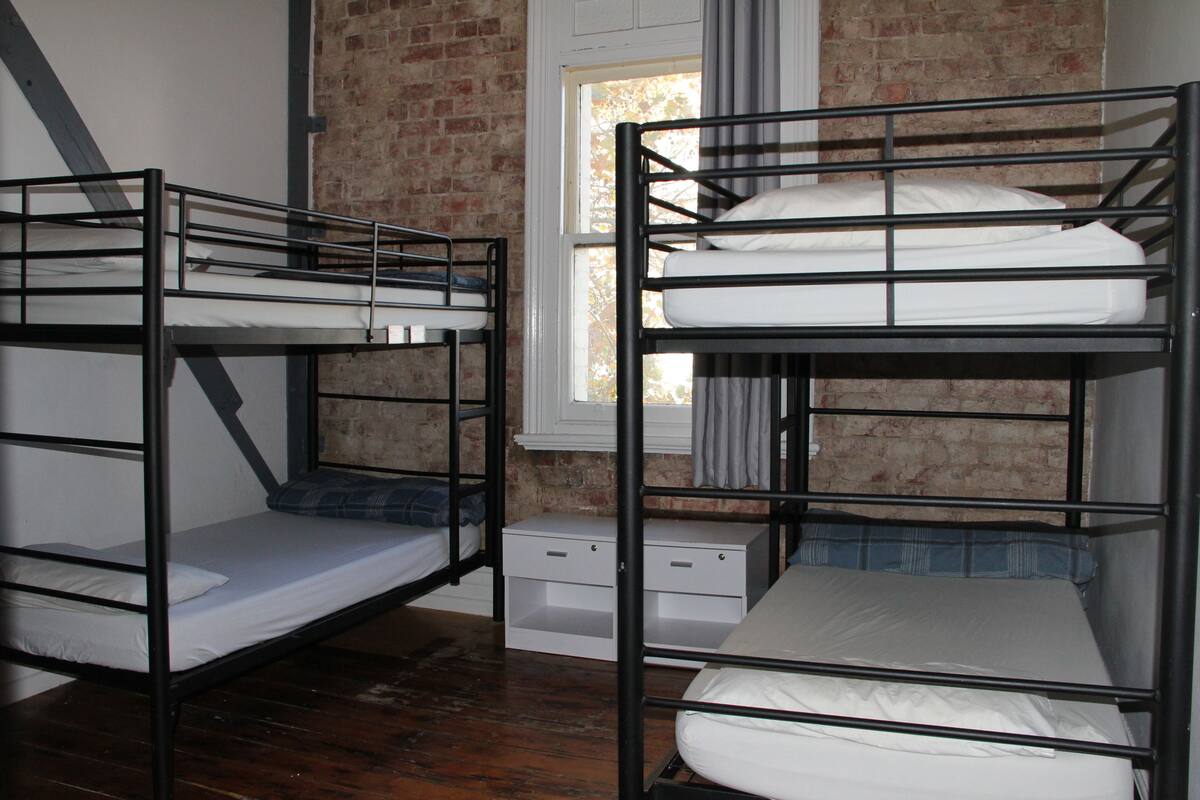 A room with two bunk beds, a small white dresser, and a brick wall.