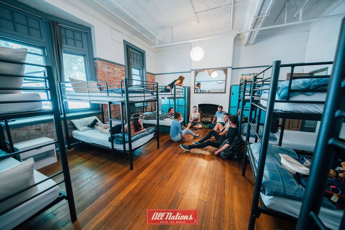 A dormitory room with bunk beds, wooden floors, and a brick wall.