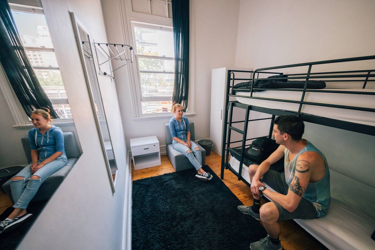A dormitory room with bunk beds, a small desk, and a window with curtains.