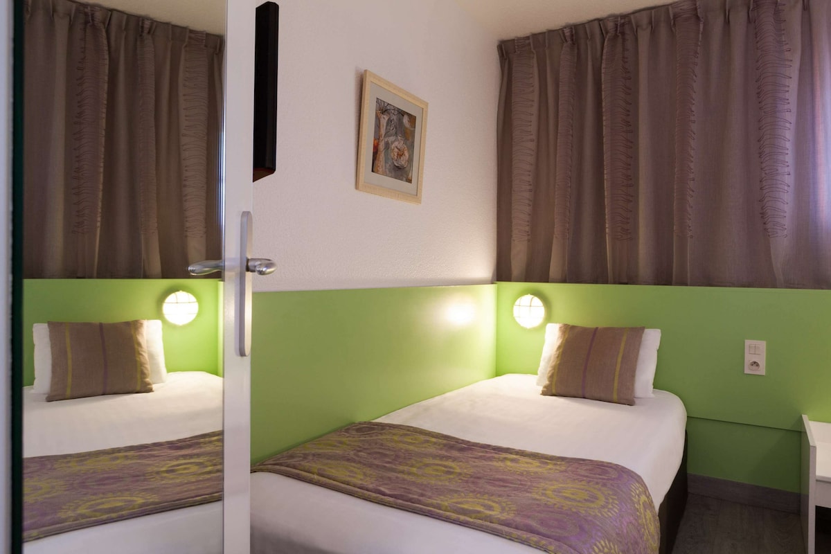 A hotel room with two beds, green walls, and a painting on the wall.