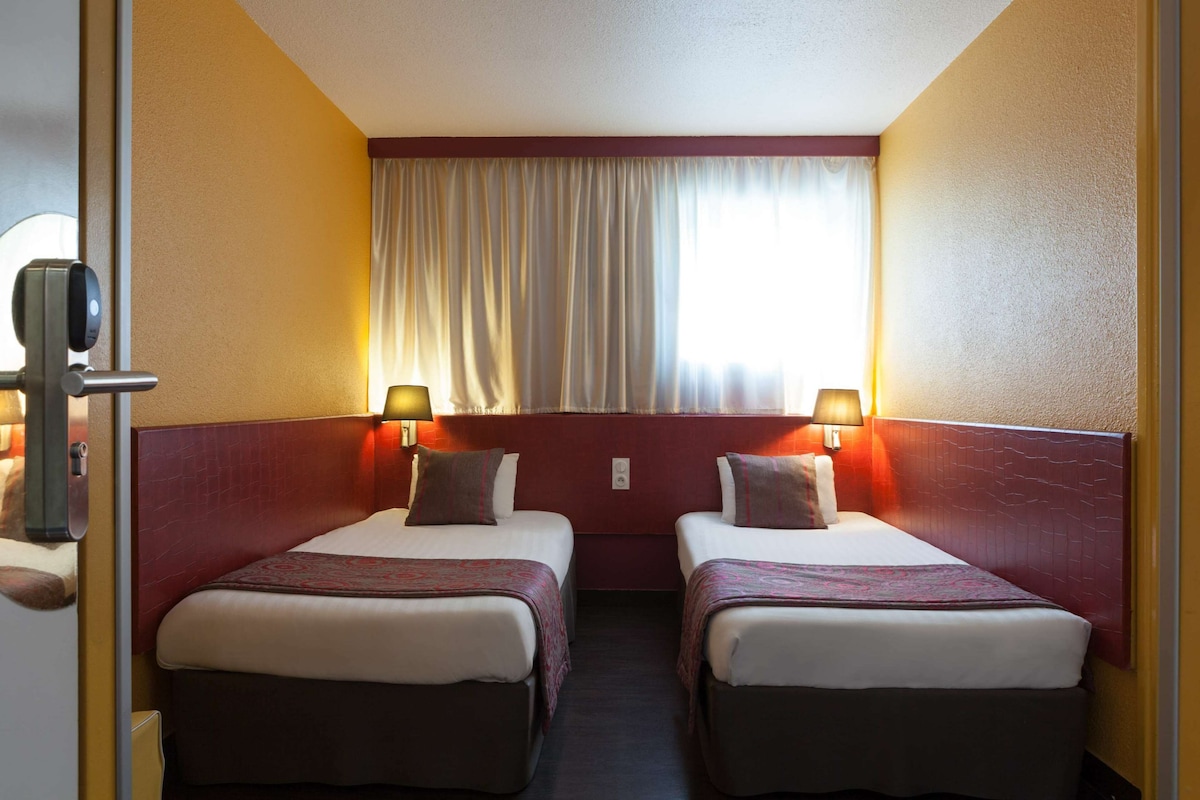 A hotel room with two beds, a window with curtains, and a door with a lock.