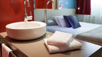 A hotel bathroom with a round sink, a towel, and a bed with pillows.