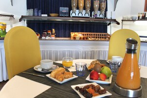 Uma mesa de café da manhã com croissants, frutas e uma cafeteira.