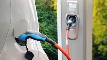 Een elektrische auto wordt opgeladen bij een laadstation, met herfstkleurige bomen op de achtergrond.