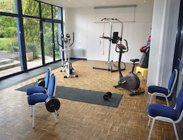 Uma academia com equipamentos de exercícios, um banco de musculação e cadeiras azuis.