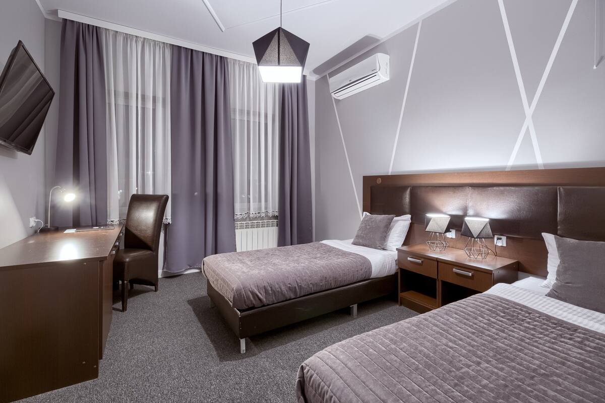 A hotel room with a bed, bedside tables, a desk, a chair, and a TV mounted on the wall.