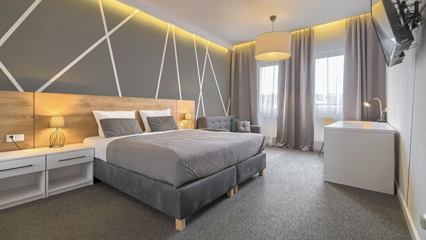 Una habitación de hotel moderna con una cama grande, mesitas de noche, un escritorio, un televisor y una ventana con cortinas.