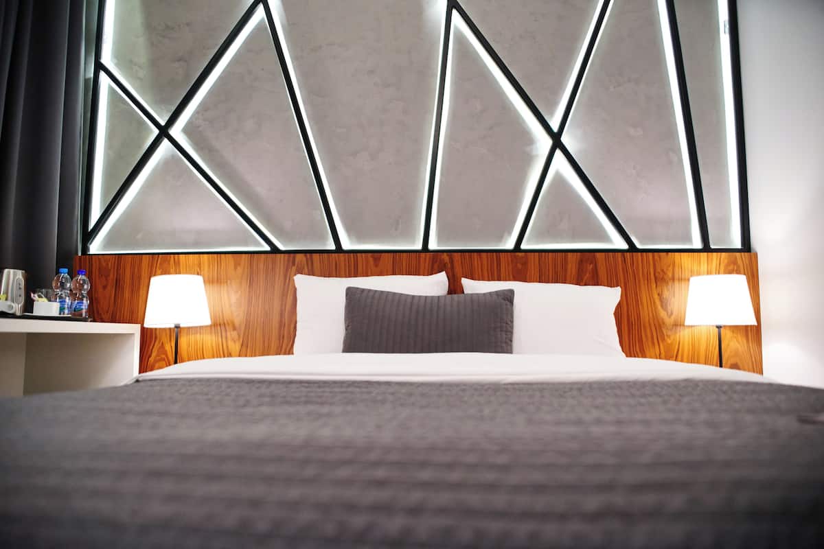 A hotel room with a large bed, two bedside lamps, a wooden headboard, and a modern geometric wall design.