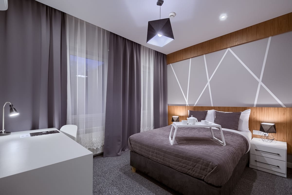 A modern hotel room with a large bed, a desk, and a nightstand.