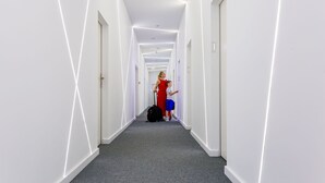Un pasillo moderno en un hotel, con distribución lineal, paredes blancas y alfombra gris.