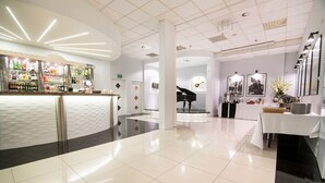 Un moderno vestíbulo de hotel con una zona de bar, un piano y obras de arte enmarcadas en las paredes.