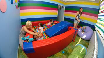Playful space with a ball pit and slide, surrounded by toys and a striped pattern.