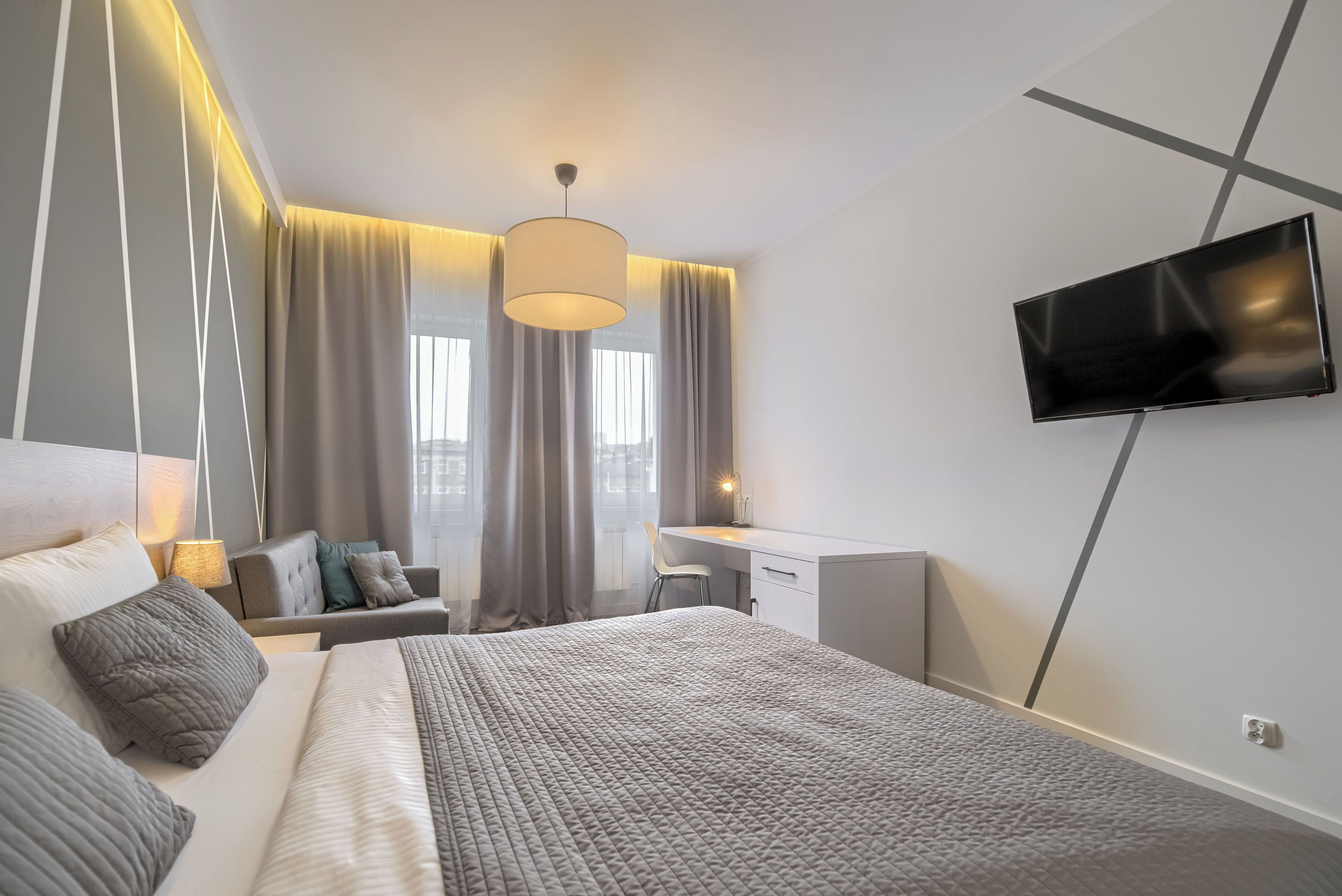 A modern hotel room with a large bed, a desk, and a TV mounted on the wall.