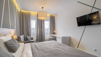 A modern hotel room with a large bed, a desk, and a TV mounted on the wall.