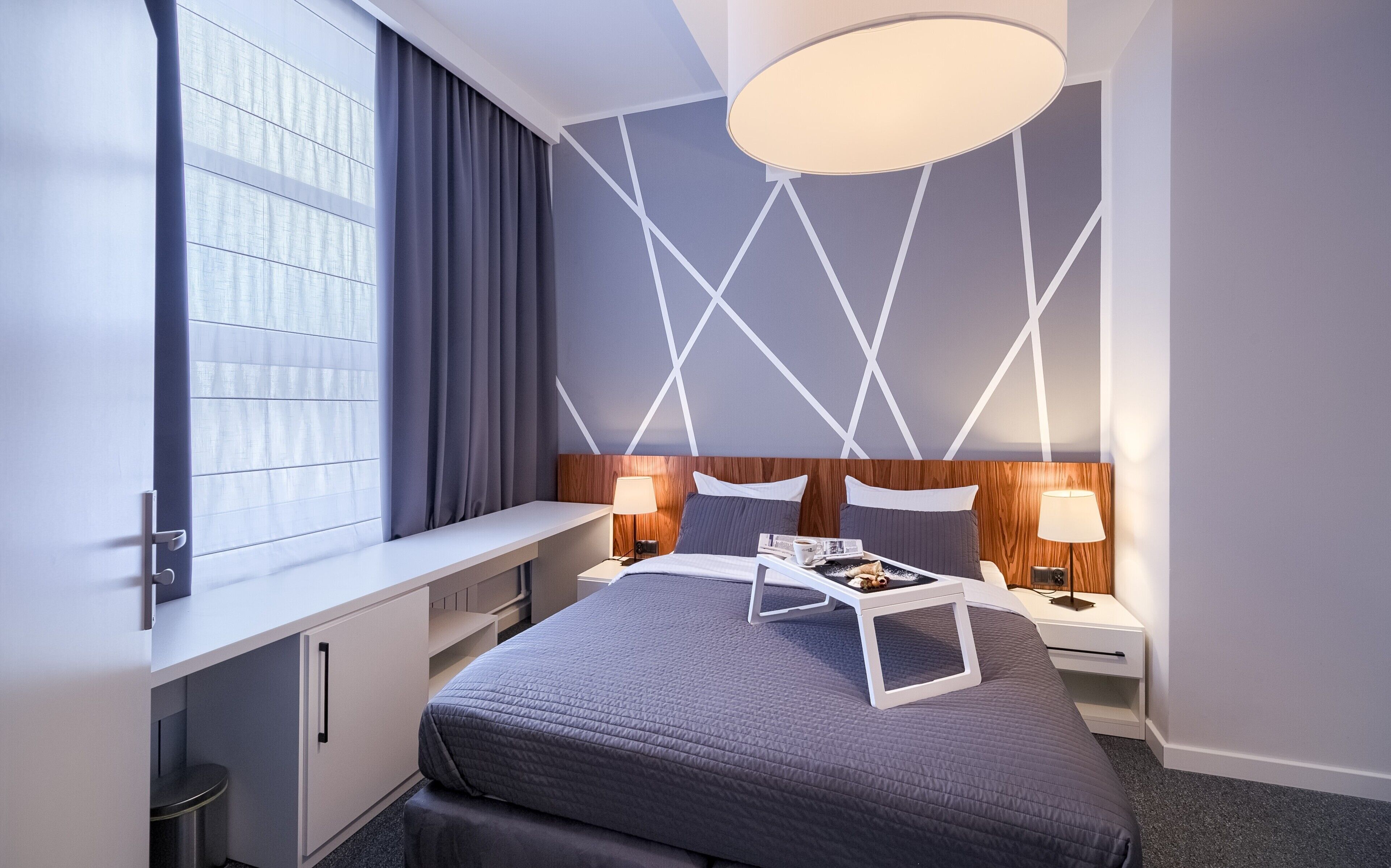 Una habitación de hotel moderna con una cama grande, mesitas de noche, un escritorio y una ventana con cortinas.