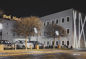 Un hotel con fachada moderna, múltiples ventanas y un estacionamiento con varios coches.