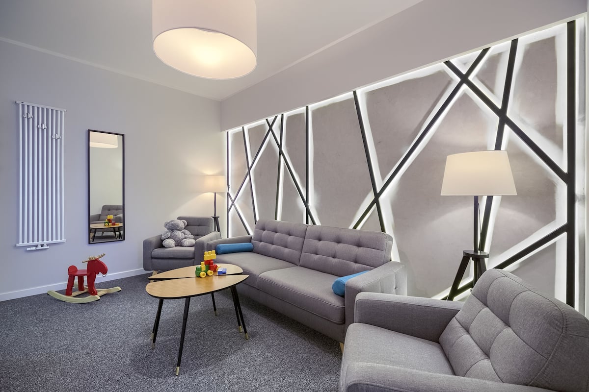 A modern living room with a sectional sofa, a small table, and a lamp. There is a radiator and a mirror on the wall.