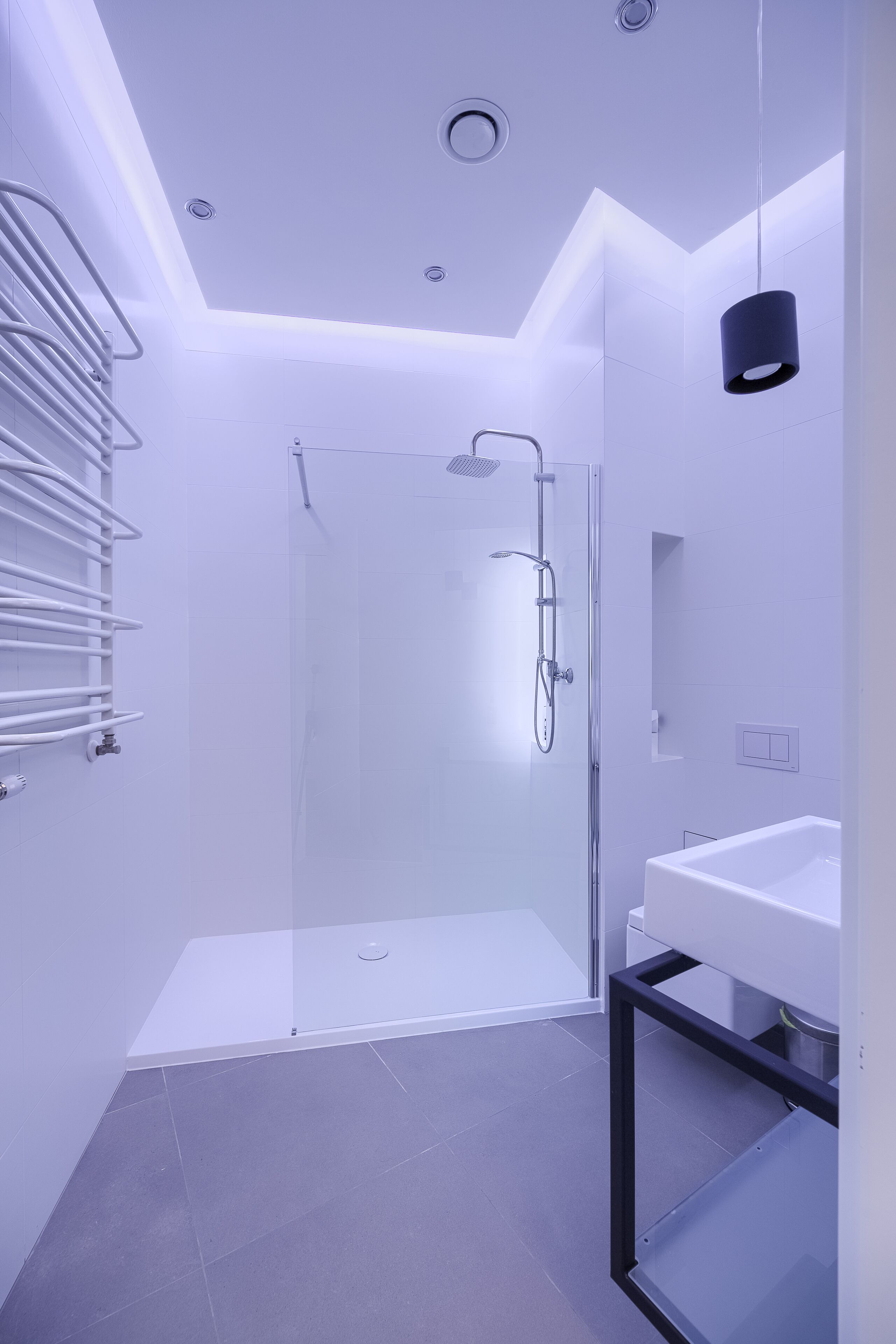 Un baño moderno con cabina de ducha de vidrio, un lavabo blanco y un perchero para toallas.