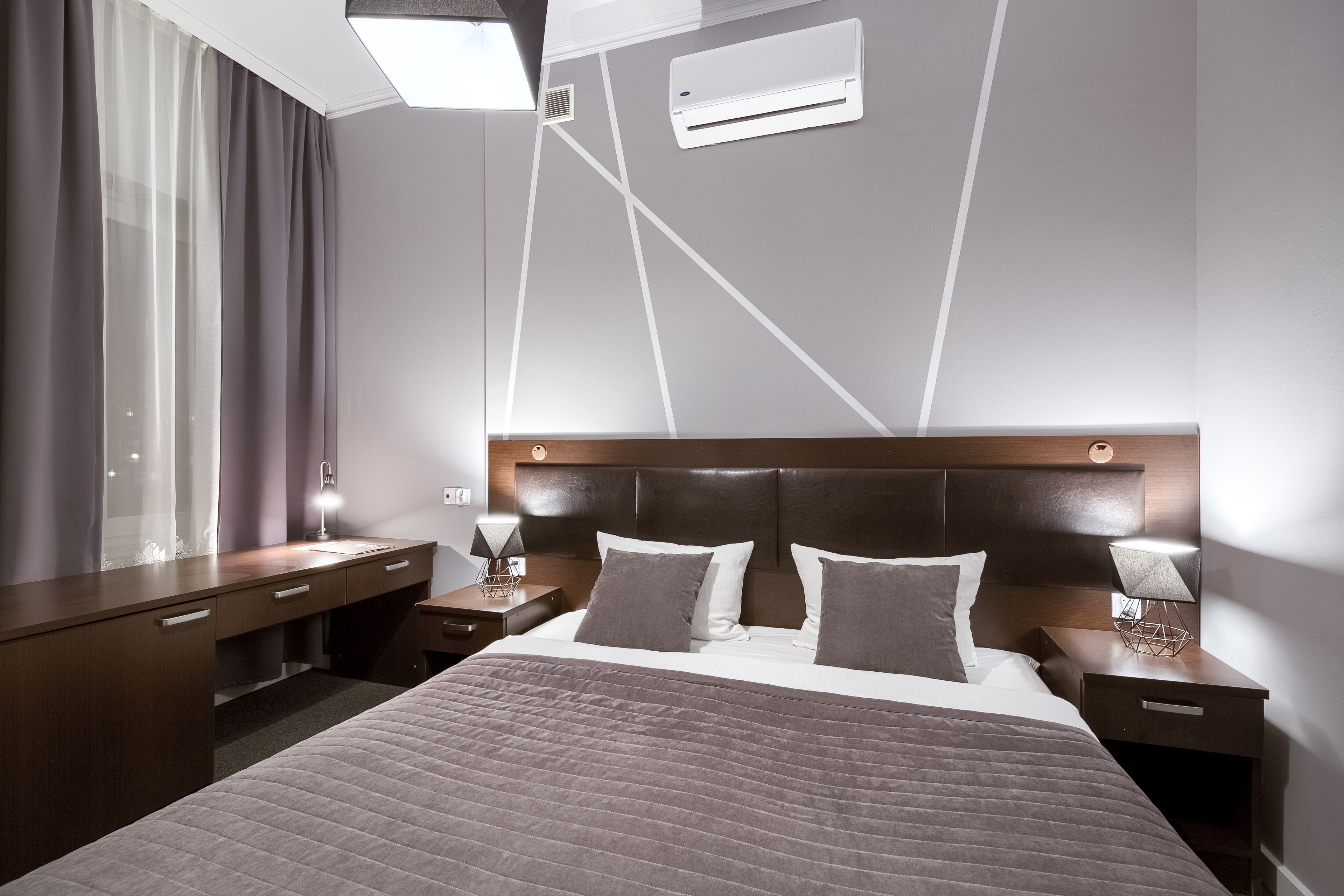 Una habitación de hotel moderna con una cama grande, mesitas de noche, un escritorio y una ventana con cortinas.