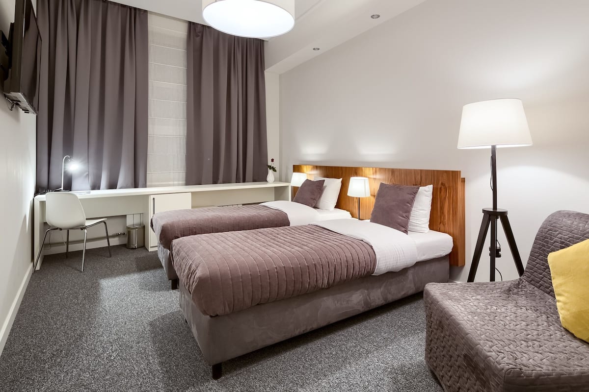 A hotel room with two beds, a desk, a chair, a lamp, and a couch.