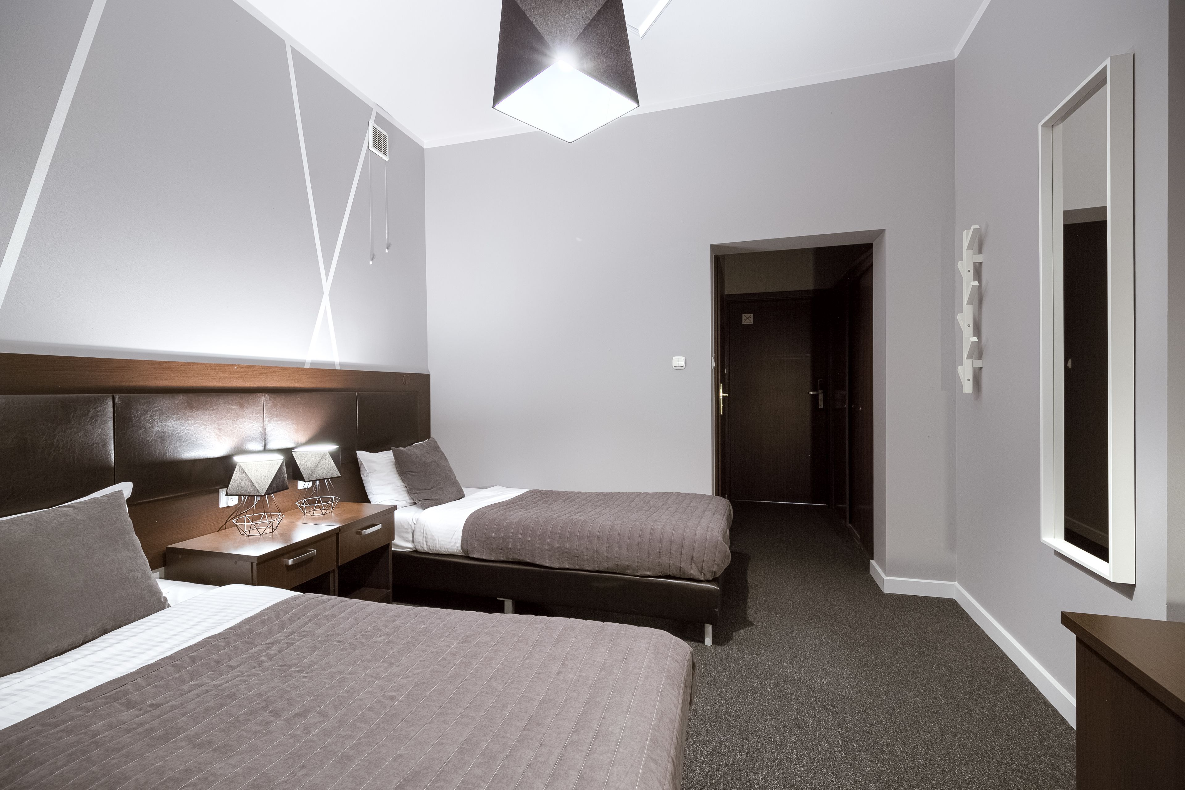 A hotel room with two beds, a nightstand with lamps, a wooden headboard, a large window, and a door leading to a bathroom.